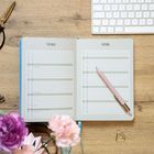 Offener Kalender mit den Überschriften „März“ und „April“; pinker Stift liegt darauf, daneben eine Tastatur und Blumen.