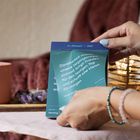 Text: "Dankbarkeit macht unsere Vergangenheit sinnvoll, bringt Frieden für den heutigen Tag und schafft eine Vision für morgen."

In einem gemütlichen Raum hält eine Person ein Kalenderblatt. Im Hintergrund sind ein Beistelltisch mit Amethyst und eine brennende Kerze zu sehen.