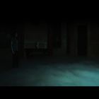 Zwei Personen in einem dunklen Raum mit Nebel auf dem Boden, eine schaut in einen verschwommenen Spiegel.