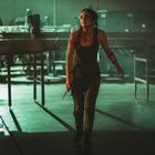 Eine kämpferisch wirkende Person geht in dunkler Fabrikumgebung, hält ein Messer, sieht entschlossen aus. Beleuchtung ist schattig.