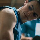 Kein Text ersichtlich. Ein junger Mann in einem ärmellosen blauen Shirt beugt sich nach vorne und betrachtet etwas interessiert.