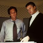 Zwei Männer in Hemden stehen nebeneinander und schauen konzentriert auf etwas Helles vor ihnen.