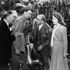 Vier Personen in einem Gespräch. Ein Mann trägt einen Cowboyhut, während ein anderer gestikuliert. Eine Frau schaut ernst.