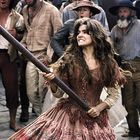 Ich kann den Texten im Bild nicht folgen, aber es zeigt eine Frau in historischer Kleidung mit entschlossener Haltung. Andere protestieren um sie herum.