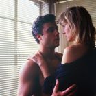 Ein Mann und eine Frau stehen sich nahe gegenüber, umarmt vor Fenstern mit Jalousien.