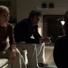 Eine Frau und ein Mann sitzen angespannt auf einem Sofa in einem Wohnzimmer, gegenüber einer dunklen Silhouette.