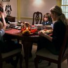 Eine Familie sitzt an einem Tisch beim Essen. Im Hintergrund ein Hund auf einer Decke und ein leuchtendes Kerzenarrangement.