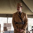 Ein Mann in khakifarbener Uniform mit Mütze steht in einem Zelt. Um ihn herum sind Kisten und Schubladenkommoden.