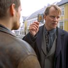 Ein Mann zeigt einen Polizeiausweis mit "POLITI" darauf, spricht mit einem anderen Mann. Hintergrund: gelbes Gebäude.