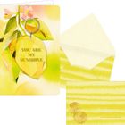 „SHINE ON“ steht auf einem runden Anhänger. Bunte Blumen schmücken die Karte, daneben ein gelber Umschlag.