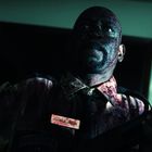 Der Text "Charlie Wells" ist auf einem Namensschild zu sehen. Ein Mann in Uniform, mit Blutflecken und einer Waffe.