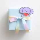 Ein pastellblaues Geschenk mit einem regenbogenfarbenen Band und einer Elefanten-Illustration, die ein rotes Herz hält.