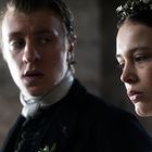 Zwei Personen in historischer Kleidung blicken ernst; eine Frau trägt Blumen im Haar.