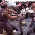 Ich kenne die Texte nicht. Eine Person tritt dynamisch auf zwei Gegner ein, die in traditioneller Kleidung posieren.