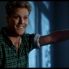 Ein Mann mit lockigem Haar und kariertem Hemd steht lächelnd an einem Türrahmen und schaut nach rechts.