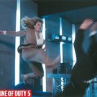 IN THE LINE OF DUTY 5: Frau in braunem Anzug tritt in die Luft, ein Mann weicht aus; futuristischer, bläulicher Raum.