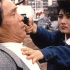 Eine Frau in blauer Jacke hält einen Mann an der Kehle; ihre Gesichtsausdrücke sind ernst und angespannt.