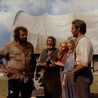 Fünf Personen stehen vor einem Planwagen. Zwei Männer unterhalten sich, während drei Personen interessiert zuhören.