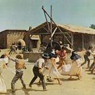 Eine Gruppe von Menschen kämpft in einem staubigen, ländlichen Dorf vor Strohhütten.