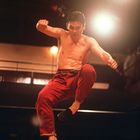 Ein Mann in roter Hose springt hoch, seine Fäuste sind geballt, in einer beleuchteten Kampfarena.