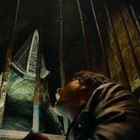 Keine sichtbaren Texte. Ein Mann schaut entsetzt durch Gitterstäbe auf eine monströse Gestalt mit pyramidenförmigem Helm.