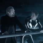 Zwei Männer stehen an einem Geländer in einer futuristischen, blauen Umgebung. Einer trägt einen Anzug mit leuchtenden Linien.