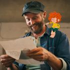 Ein Mann liest lächelnd einen Brief. Auf seiner Schulter sitzt eine animierte Figur mit rotem Haar.