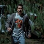 Ein Mann trägt ein T-Shirt mit Comic-Aufdruck. Er läuft in einem dunklen Wald, umgeben von Bäumen.