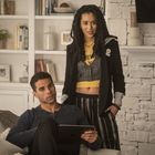 Ein Mann sitzt auf einem Sofa mit einem Tablet. Eine Frau steht neben ihm und trägt ein gelbes Oberteil mit Aufdruck. Im Hintergrund ein Bücherregal.