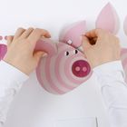 Hände setzen ein Schweinegesicht aus rosa-weißen Papierelementen zusammen, mit kreisförmigem Schnauzendetail.