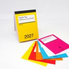 Ein gelber Tageskalender für 2027 von Reclam, "Tag für Tag Weltliteratur zum Abreißen". Bunte Blätter liegen daneben.
