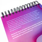 Text auf einem lilafarbenen, spiralgebundenen Kalender. Es beschreibt prominente Personen und Lebensweisheiten.