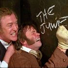 Die Worte "THE JUWES" sind an eine Wand gekritzelt. Zwei Männer wirken aufgeregt und lachen.