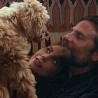 Eine Frau und ein Mann kuscheln auf einem Teppich mit einem flauschigen Hund, der vor ihnen steht.