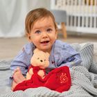 Ein lächelndes Kleinkind in blauem Hemd hält einen Kuschelteddy mit rotem Tuch, darauf ist ein Bienenstock abgebildet.