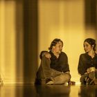 Ich kann den Text nicht erkennen. Eine Frau und ein Mann sitzen nebeneinander auf dem Boden, neben ihnen eine Flasche und eine Leiter.