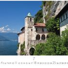 „Santa Caterina del Sasso“ steht oben links. Ein Kloster thront auf einem Felsen über einem See, umgeben von Bergen und Bäumen.