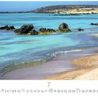 "Südküste", darunter ein Kalender für Juli. Eine Küstenlandschaft mit türkisblauem Wasser, Felsen und Sandstrand.