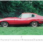 „Jaguar E-Type“, Monatskalender Juli mit Nummern; rotes Auto auf grünem Rasen, Bäume im Hintergrund.