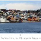 Aufschrift: "Kristiansund". Bunte Häuser auf Hügeln am Wasser, im Hintergrund eine Kirche und schneebedeckte Berge.