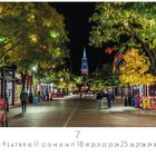 Vermont, Burlington. Eine nächtliche Straße mit beleuchteten Bäumen, einer Kirche im Hintergrund und einer bunten, lebendigen Szene.