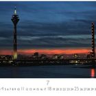 "Oberkasseler Brücke" unten links. Nächtliche Skyline mit beleuchtetem Turm und Brücke vor dunklem Himmel.
