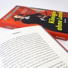 Der Text auf einer Buchseite lautet "Kapitel 2". Daneben ein Buch mit dem Titel "Königin ohne Land".