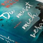 Der Text lautet "Du musst mich vergessen" und "Roman". Ein blumiges Design mit Blüten und einem blauen Hintergrund.