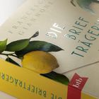 Die Worte "Die Briefträgerin" und "Francesco Giannone" stehen auf einem Buch mit Zitronen- und Blätterillustration.