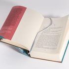 Ein aufgeschlagenes Buch mit einer roten Umschlagseite und einem blauen Buchrücken. Der Text behandelt feministische Themen.
