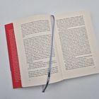 Ein aufgeschlagenes Buch mit Text auf beiden Seiten, links eingefasst von einem roten Buchrücken. Ein blaues Leseband ist sichtbar.