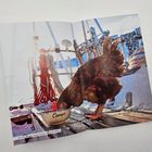 Text: „Monique“ auf einer Schüssel, die ein Huhn auf einem Boot anpickt. Schnee und Seile im Hintergrund.
