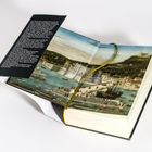 Textabschnitt über ein Königreich verteidigen. Geöffnetes Buch mit mittelalterlichem Stadtbild am Wasser; gelbes Lesezeichen.