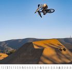 Kalenderblatt mit Nummern 1 bis 31. Ein BMX-Fahrer springt über einen Erdwall vor einem klaren Himmel und Hügeln.